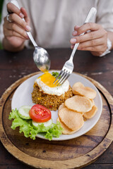 Indonesian fried rice with sunny side up egg, prawn crackers, fresh vegetables, served on a round wooden tray. Traditional Asian street food concept.