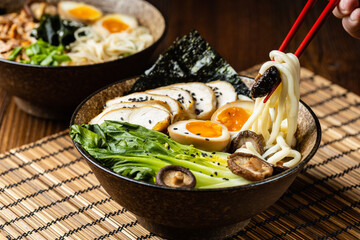 Traditional ramen with jerked pork or chicken.  With udon or ramen noodles. Served in classic bowls. Gyoza dumplings and mushrooms in the background.