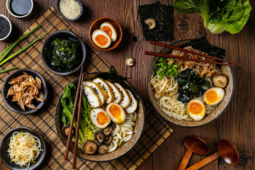 Traditional ramen with jerked pork or chicken.  With udon or ramen noodles. Served in classic bowls. Gyoza dumplings and mushrooms in the background.