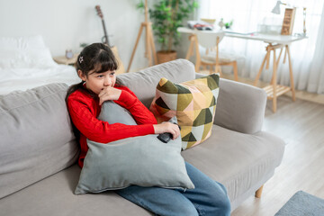 Obraz premium Asian young girl sitting on sofa and watching TV in living room at home. 