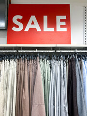 Clothing store sale with multiple pants on racks beneath a big red sale sign. The display highlights various shades and styles, enticing shoppers to explore discounts on apparel.
