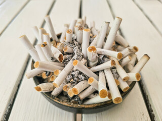 Full ashtray with many cigarette butts and ashes on a white wooden table, symbolizing smoking addiction and unhealthy lifestyle.