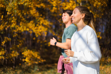 Young beautiful couple jogging in city beautiful autumn park and forest, enjoying outdoor sports