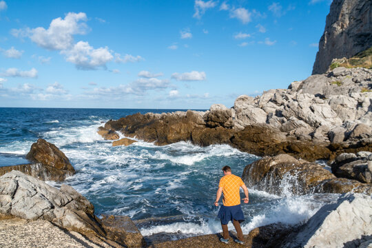 Man stands by crashing waves on rocky shore - Powered by Adobe