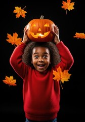 Happy black girl holding pumpkin above head, black background, autumn leaves falling. Happy Halloween	