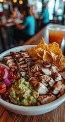 Chicken bowl with chips, guac, and beverage on wooden table