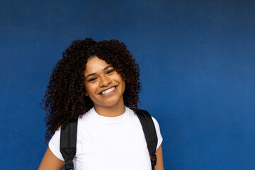 Portrait of smiling young student with backpack on blue background