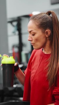 Woman in red sportswear holding protein shaker in gym after workout. Concept of fitness lifestyle, healthy nutrition, hydration, and recovery. Perfect for wellness, sport, and active lifestyle themes.