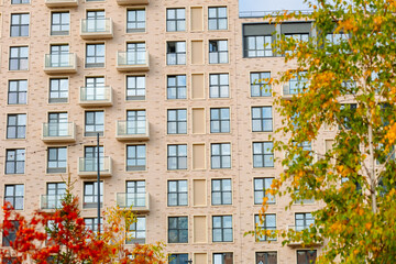 A modern residential complex with balconies, surrounded by trees. Brick walls, large windows, and cozy balconies. In autumn, the leaves turn vibrant colors, creating a cozy atmosphere.