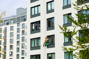 An industrial climber cleans windows on the façade of an apartment building, using safety systems and specialized equipment for working at height.