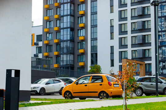 A bright yellow car is parked near a modern residential complex. The compact car stands out against the gray and white buildings with yellow accents.