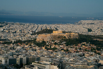 View of Athens with the Acropolis and Parthenon illuminated by the warm light of sunsrise. The historic ancient citadel rises above the modern city, 