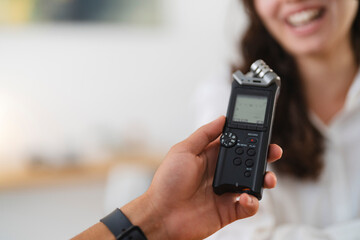A person holds a digital audio recorder to capture the voice of a smiling woman during an interview or conversation.