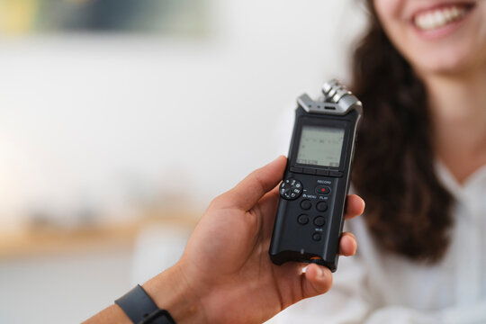 A person holds a digital audio recorder, capturing sound during an interview with a smiling woman.