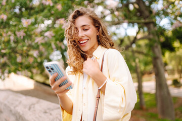 A cheerful woman with a phone takes a stroll on a sunny day. A beautiful woman enjoys the weather,...
