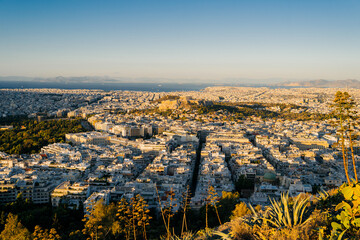 Panoramic view of Athens, Greece from the top of Lycabettus Hill at sunset. The Acropolis can be seen in the distance with the urban sprawl of the Greek capital spreading toward the horizon. White