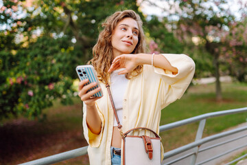 A cheerful woman with a phone takes a stroll on a sunny day. A beautiful woman enjoys the weather,...