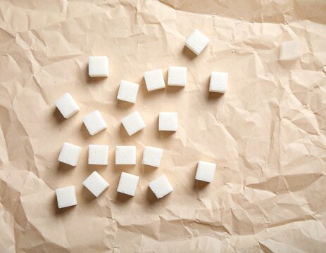 Delicate white sugar cubes thoughtfully arranged on a richly textured brown paper, their pristine form contrasting beautifully with the rustic surface, hinting at purity and sweetness