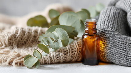 Amber essential oil bottle placed on soft knit fabric next to fresh eucalyptus leaves, natural wellness and aromatherapy concept, warm and cozy atmosphere