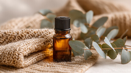 Amber essential oil bottle placed on soft knit fabric next to fresh eucalyptus leaves, natural wellness and aromatherapy concept, warm and cozy atmosphere