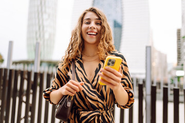 A young woman with phone enjoys life against the backdrop of urban metropolis. Beautiful tourist...