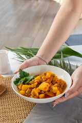 Hands serving homemade potato stew with parsley