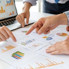 Hands pointing to charts on paper, laptop in background