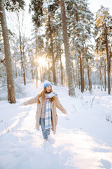 Portrait of a joyful woman with a bright scarf and hat enjoying herself in a snowy forest.  Beautiful woman enjoys a sunny winter day outdoors. Concept for relaxation and weekends.