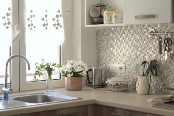 Objects and flowers, kitchen workspace with mosaic tile wall. Traditional apartment interior, Italy. Ceramic tableware and kitchenware.