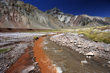 A small river flowing through a valley between mountains. A muddy mountain river flowing through a rocky gorge