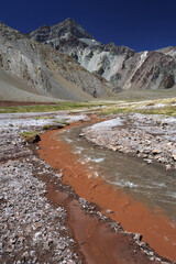 A small river flowing through a valley between mountains. A muddy mountain river flowing through a rocky gorge