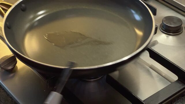 Close-up view of an empty non-stick frying pan being heated on a gas stovetop in a residential kitchen setting.