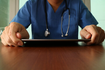 Doctor in scrubs using digital tablet with stethoscope