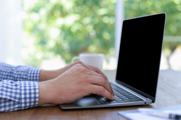 Fototapeta premium Man working on laptop at wooden table indoors, closeup
