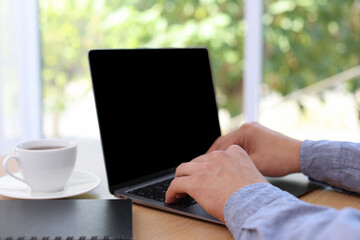 Man working on laptop at wooden table indoors, closeup