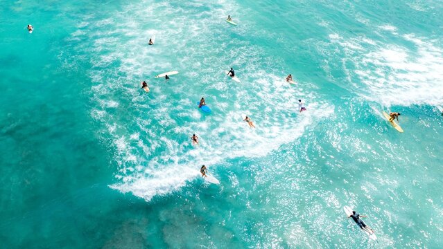 Aerial view of surfers riding the dazzling turquoise waves, a symphony of motion and light on the Pacific, Waikiki, Honolulu, Hawaii, United States.