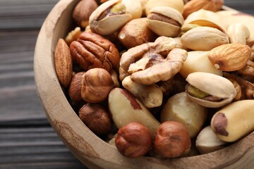 Mix of different nuts in bowl on wooden table, closeup