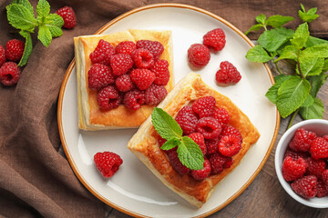 Yummy puff pastries with raspberries and mint on wooden table, flat lay