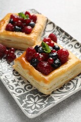 Tasty puff pastries with berries and mint on light grey table, closeup