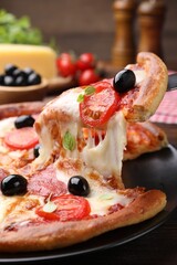Taking piece of delicious pizza with cheese, salami, tomatoes and olives at table, closeup