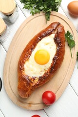 Tasty khachapuri with cheese, eggs and other products on white wooden table, flat lay