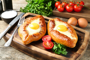 Tasty khachapuris with cheese and eggs served on wooden table, closeup