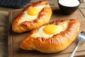 Tasty khachapuris with cheese and eggs served on wooden table, closeup