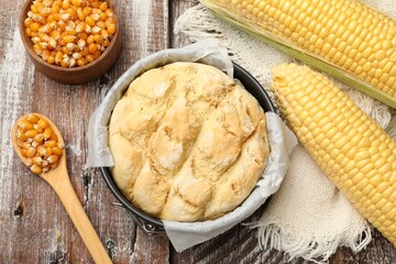 Freshly baked cornbread in cake pan, cobs and spoon on color wooden table, flat lay