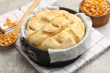 Freshly baked cornbread in cake pan, seeds and spoon on grey textured table, closeup