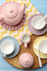 Beautiful ceramic tea set for children and napkin on light blue wooden table, top view