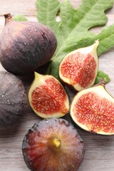 Fresh ripe figs and green leaf on wooden table, flat lay