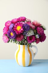 Beautiful flowers in vase on light blue wooden table against grey background