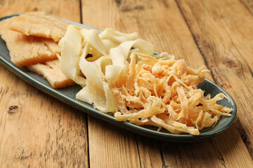 Different tasty dried squid on wooden table, closeup