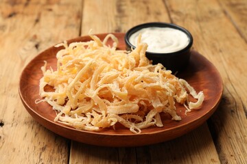 Tasty dried squid shavings and sauce on wooden table, closeup
